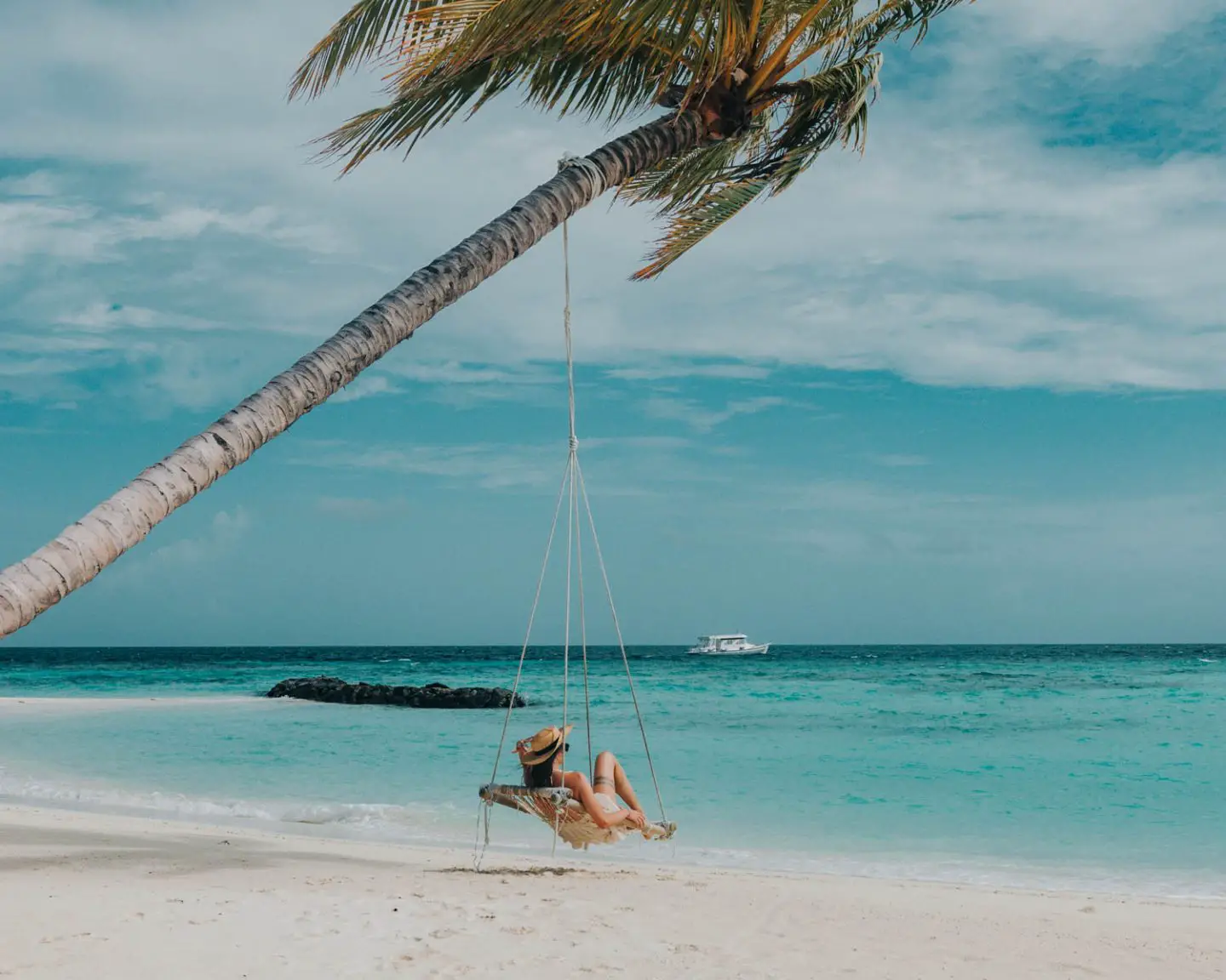 girl sitting on palm tree swing in maldives